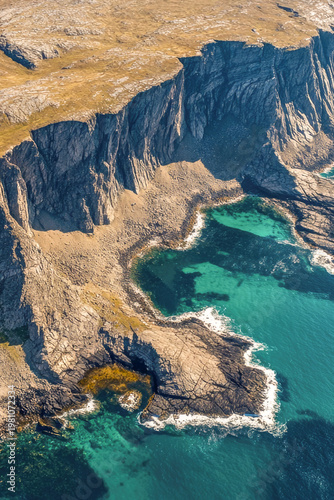 Aerial view of a rocky coastline with blue water, suitable for use in travel or landscape photography. vertical frame