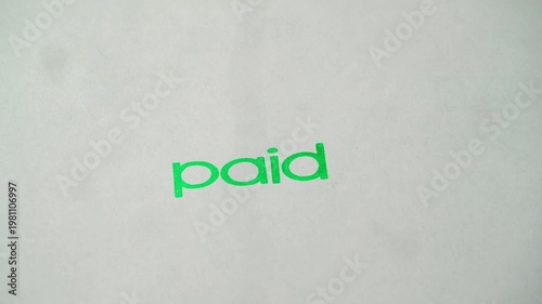 Rubber stamp prints paid text in green ink over empty white document during payment verification.