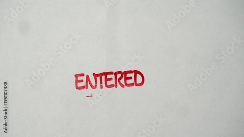 Rubber stamp prints entered text in red ink over empty white document during entry verification.