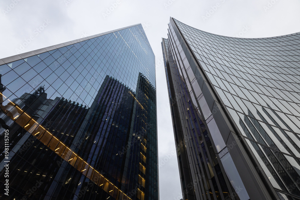 Fototapeta premium Looking up at towering glass office buildings against a cloudy sky