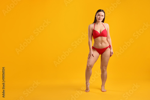 Beautiful woman in stylish swimsuit posing on yellow background. Space for text