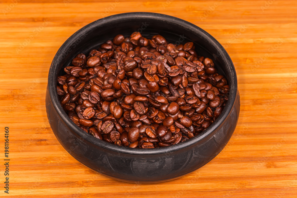 Fototapeta premium Roasted coffee beans in black clay bowl on wooden surface