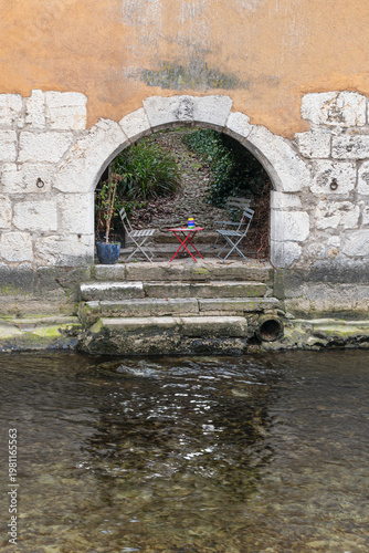 Chairs and table under archway in ancient wall at the river Le Thiou in Annecy France in portrait format