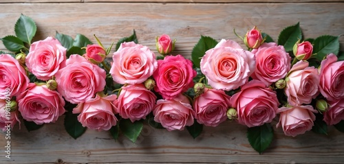 Many pink roses and buds arranged on a rustic wooden background. This floral display features lush petals and green leaves. Perfect for wedding invitations, gift cards, or beauty blogs.