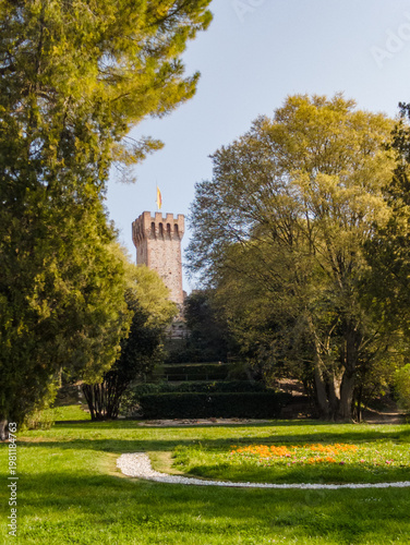 Visit Este Castle in Padua, Italy, to see the historic tower surrounded by lush trees and colorful flowers in springtime
