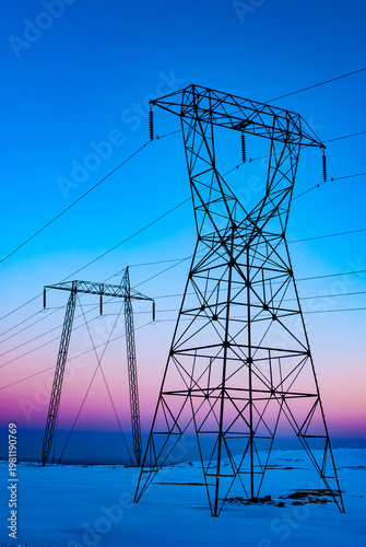 Power lines and transmission towers silhouetted against sunset sky in Iceland. Industrial Iceland scene with energy infrastructure, cables, and warm evening light.