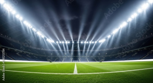 A low angle view of a football stadium pitch at night with bright floodlights shining overhead