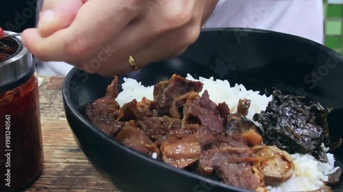 A hand adding chili paste to a bowl of braised beef (Ngau Lam) with Chu Hou paste, fermented spinach and rice. A traditional local Cantonese dish. Central, Hong Kong