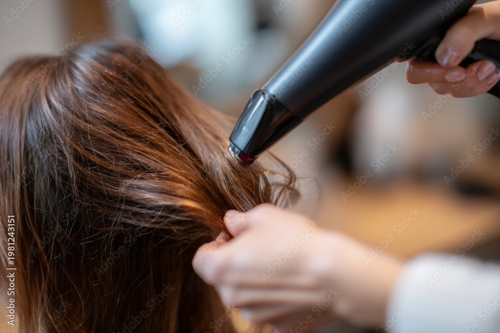 Naklejka premium Close-up of a hairdresser drying woman's brown hair with a black blow dryer. Professional beauty salon styling service