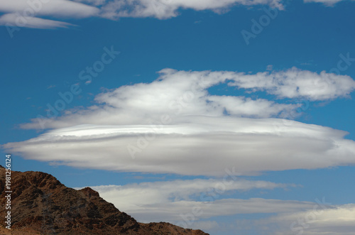 Large lenticular cloud forming above the Mojave Desert on a windy day with clear blue skies in California.