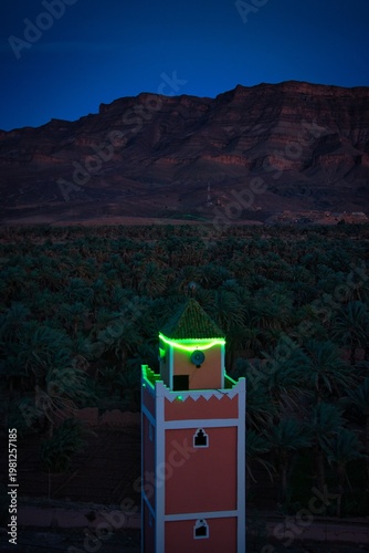 Illuminated minaret green light at blue hour Morocco oasis
