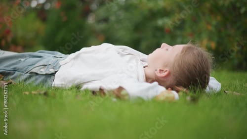 Child lying on lawn gazing at sky soft profile framed by green foliage serene afternoon portrait daydreamer imagining stories gentle breeze closeup composition intimate perspective