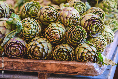 A rustic display of fresh green artichokes stacked in a wooden crate at a market