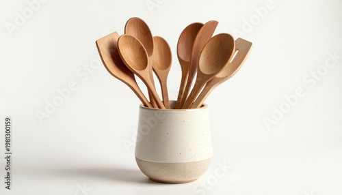 Wooden kitchen tools set in ceramic holder. Spatulas and spoons stand together on white background. Essential cookery equipment for food preparation.