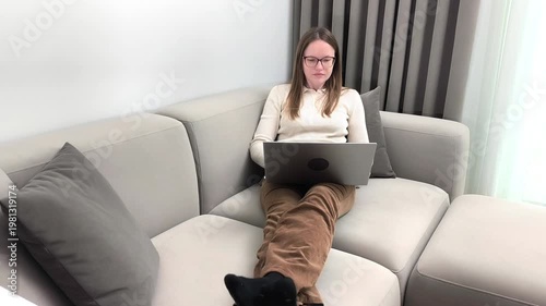 Laptop preparation starts as woman on sofa opens device to begin online task. Female gets ready for remote work session at home. Digital lifestyle concept with freelance activity indoors..