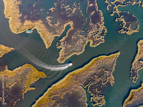 Aerial view of Dalyan River Delta with boats moving through winding channels and wetlands. Natural patterns, marsh ecosystem, tourism activity, water landscape and environmental conservation concept. 