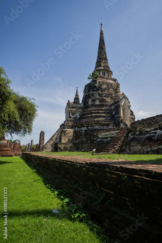 Vászonkép Row of ancient chedis and stupas with lush green lawn at Ayutthaya Historical Park, Thailand, under a bright blue sky with white clouds