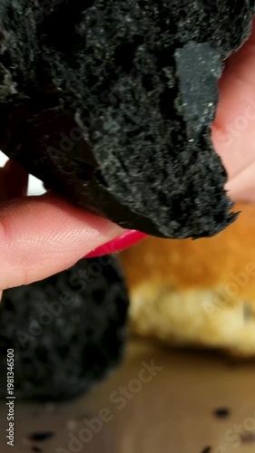 Black bun texture breaking and squeezing soft bread structure close-up bakery product on beige plate food detail concept