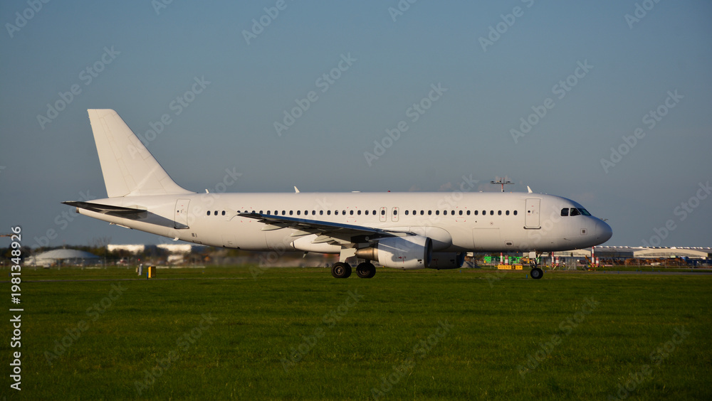 Obraz premium Airbus A320-200 in an all white and blank livery during sunset on green gras