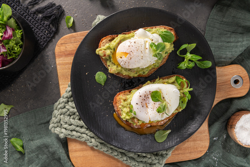 Wallpaper Mural Flat lay of two sourdough toasts topped with mashed avocado and soft poached eggs on a black plate with vibrant golden yolk dripping onto the surface and a side of fresh garden salad Torontodigital.ca