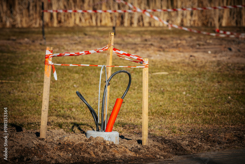 Construction site with safety barriers surrounding a newly installed utility pole and cables on a grassy area, indicating ongoing infrastructure work