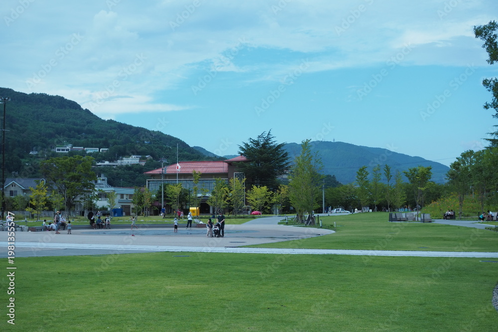 Fototapeta premium Family Relaxing in Green Park with Mountain View 家族が過ごす緑豊かな公園と山の風景