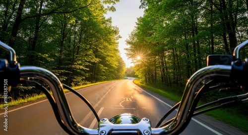 Point of view over metallic handlebars onto a curving rural road surrounded by green trees and golden sunlight at the end of the day, destination, riding, adventure