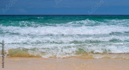 A sandy beach on the coastline of the ocean with clear water with small waves.