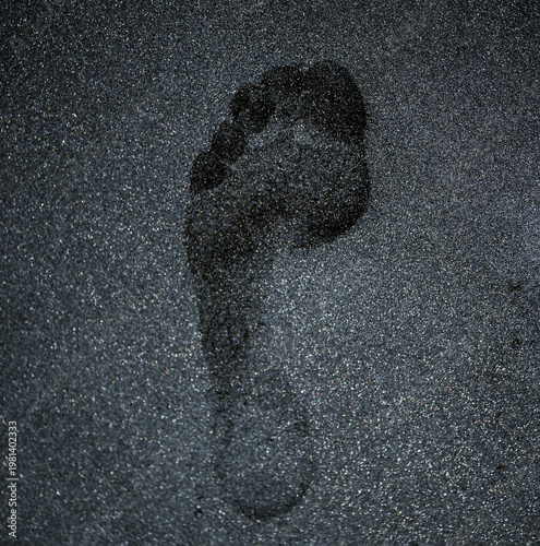 Footprint on black volcanic sand, close-up of a person step on the beach.