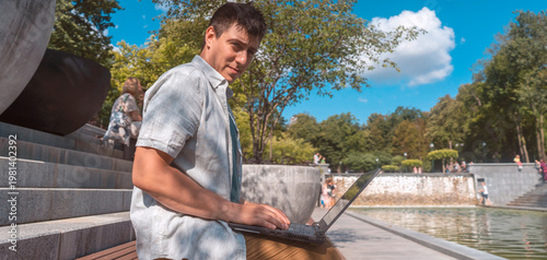 A man is working on a laptop, typing on a keyboard outdoors.