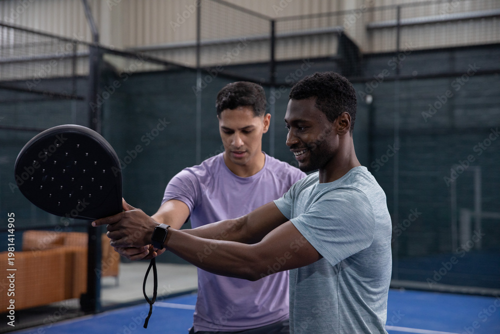 Fototapeta premium Coaching coach guiding trainee in athletic shirts on blue court, showing paddle grip and smartwatch