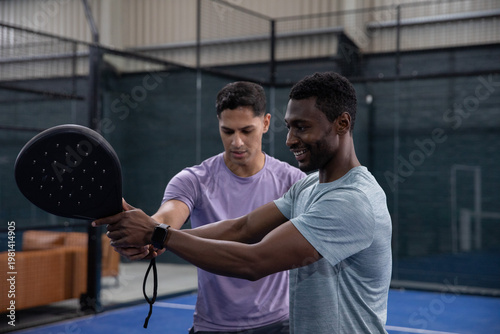 Coaching coach guiding trainee in athletic shirts on blue court, showing paddle grip and smartwatch