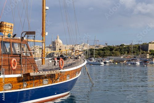 Tablou pe pânză Classic Wooden Sailboat Moored in Msida Marina with Valletta Cathedral Dome Skyl