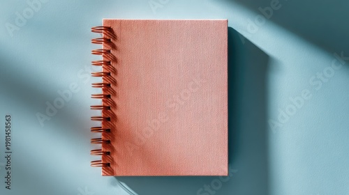 Pink Spiral Notebook on Blue Surface with Soft Light and Shadow Highlighting Texture and Design Elements for Creative and Professional Use