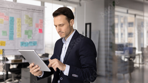 Virtual project management. Focused busy mid adult male business specialist work on digital pad in office manage tasks in online planning app use ai to check risks create ideas set goals for sprints