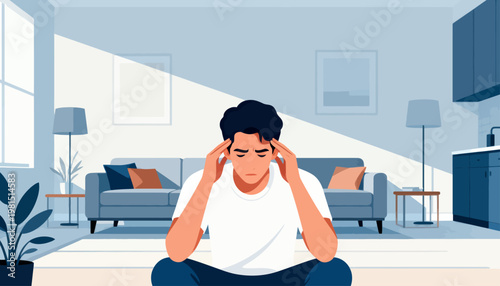 Young man sits on floor, hands on head. He looks stressed, eyes closed, fingers pressed to temples. Modern living room has soft lighting and minimalist decor