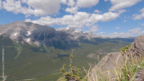 Scenic summer mountain landscape with dramatic rocky peaks, green forest valleys, and blue sky with clouds. View from a hiking trail overlooking the Canadian Rockies, capturing nature, adventure, and 