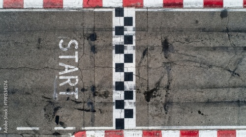 Overhead view of asphalt racetrack starting line with white checkered markings and red white borders.