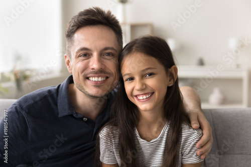Cuadro en lienzo Close up portrait handsome dad posing seated on sofa with little daughter