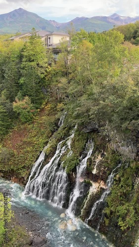 Shirahige Waterfall with deep cobalt blue hue, Waterfall of Shirahige and Tokachidake Mountain Range in Biei-cho, Hokkaido Japan in early fall or autumn season. famous tourist destination in Biei