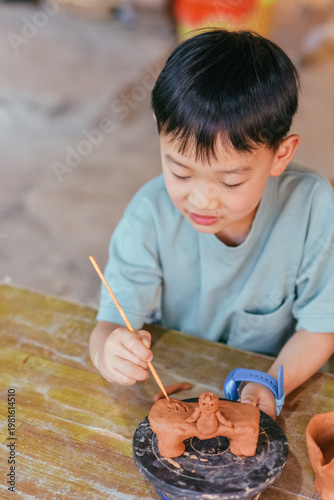 Young Asian boy experiencing traditional Dai pottery making at Manzhang Village, Xishuangbanna, Yunnan, China