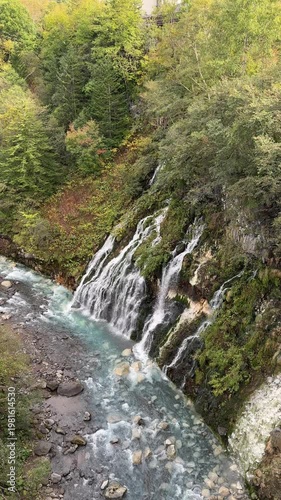 Shirahige Waterfall with deep cobalt blue hue, Waterfall of Shirahige and Tokachidake Mountain Range in Biei-cho, Hokkaido Japan in early fall or autumn season. famous tourist destination in Biei