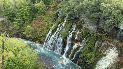 Shirahige Waterfall with deep cobalt blue hue, Waterfall of Shirahige and Tokachidake Mountain Range in Biei-cho, Hokkaido Japan in early fall or autumn season. famous tourist destination in Biei