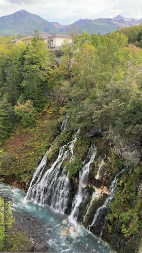 Shirahige Waterfall with deep cobalt blue hue, Waterfall of Shirahige and Tokachidake Mountain Range in Biei-cho, Hokkaido Japan in early fall or autumn season. famous tourist destination in Biei