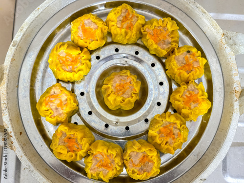 homemade chicken dimsum being steamed in a stainless steel steamer pot on a gas stove. Traditional Asian dumplings with carrot topping cooked until tender and ready to serve. top view