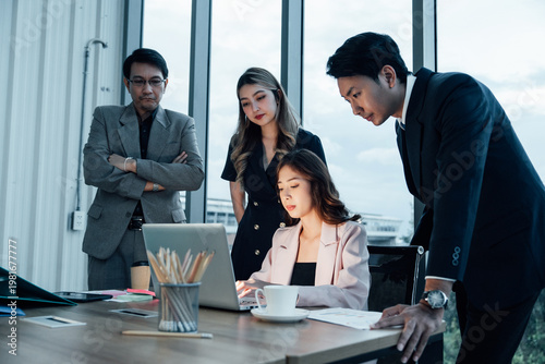 Fotografia Two Asian colleagues intently observe a laptop and detailed documents in a modern office, collaborating on a business project while wearing business attire and conveying a serious mood