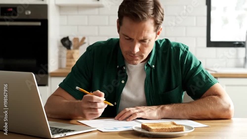Wallpaper Mural Focused Man Working From Home in a Bright Kitchen Using a Laptop and Writing Notes While Eating Breakfast Toast Torontodigital.ca