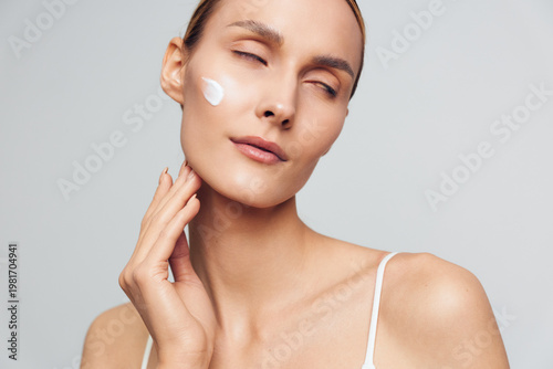 Woman skincare beauty portrait with cotton pad and moisturizer, self care for healthy skin in a spa style close up, calm female face, grey studio background soft light care
