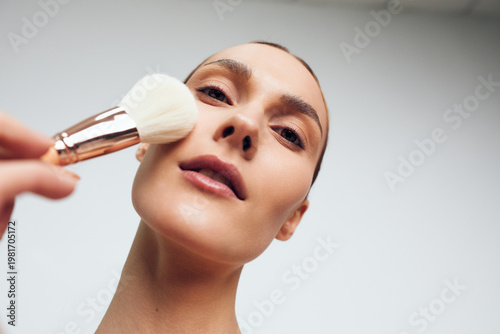 Woman in a beauty spa gets facial makeup applied with a soft brush, calm closeup of her face and skincare, clean background, professional cosmetic treatment care concept