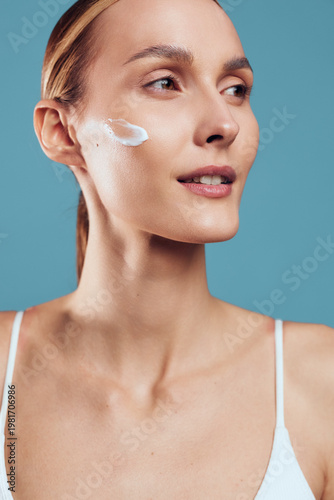 Woman skincare face cream close up blue background self care wellness beauty applying moisturizer, calm smile, spa routine, soft studio lighting, healthy skin hydration